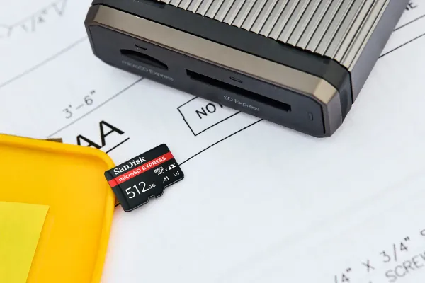 A SanDisk microSD Express memory card on a desk next to a card reader