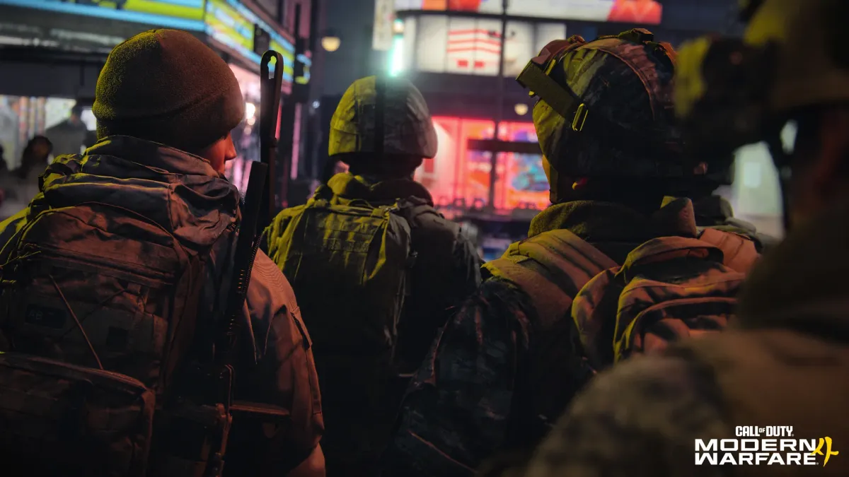 A squad of soldiers seen from behind, moving down a city street at night lit by neon signs, with the Call of Duty Modern Warfare 4 logo in the bottom-right corner